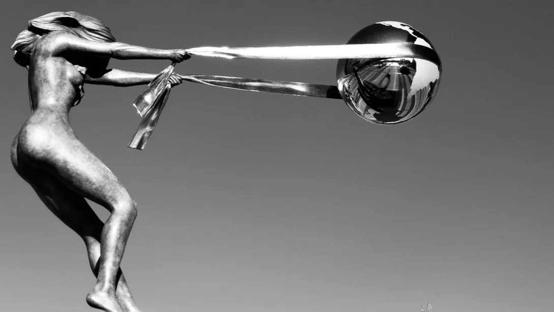 Black-and-white photo of a statue of a woman pulling a long ribbon from a mirrored sphere.